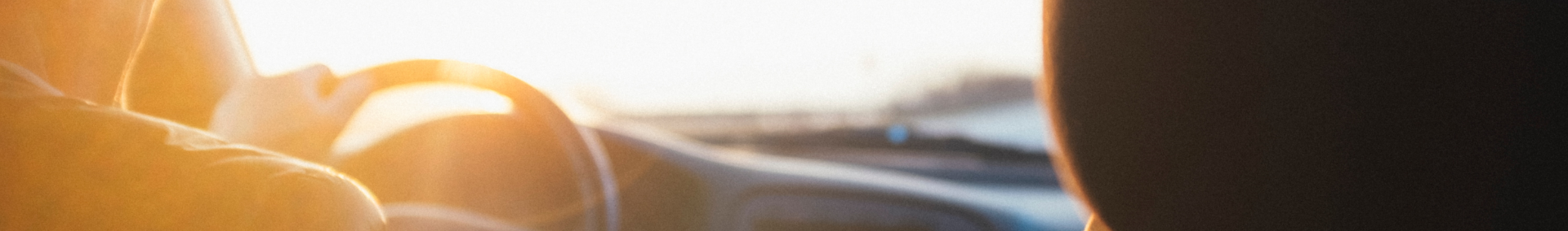 driver in the car with hands on steering wheel at sunset